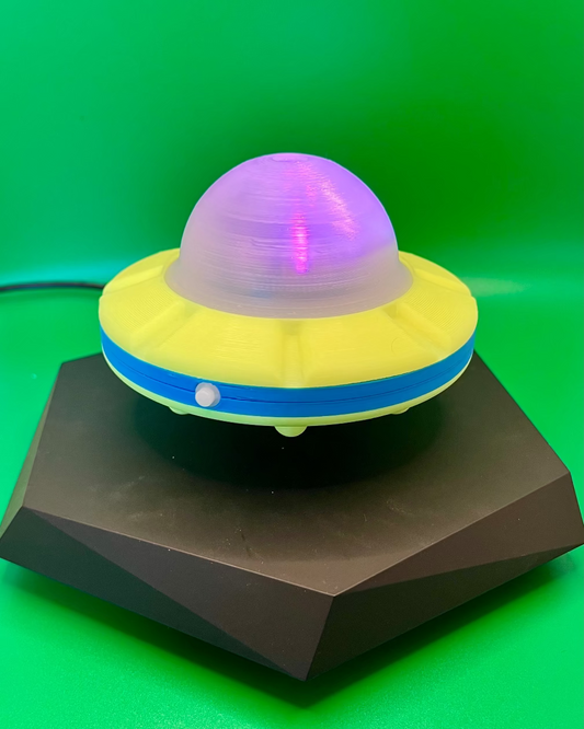 Toy UFO with purple top on a black stand against a green background